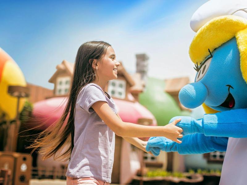 Fille dans un parc d'attractions tenant la main d'un personnage de dessin animé bleu avec un chapeau jaune.