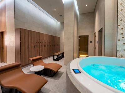 Moderní wellness prostor s vířivkou a pohodlnými lehátky vedle dřevěných skříněk a tlumeného osvětlení.