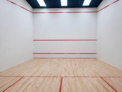 Prázdný kurt na squash s dřevěnou podlahou, bílými stěnami a červenými herními čarami pod jasným stropním osvětlením.