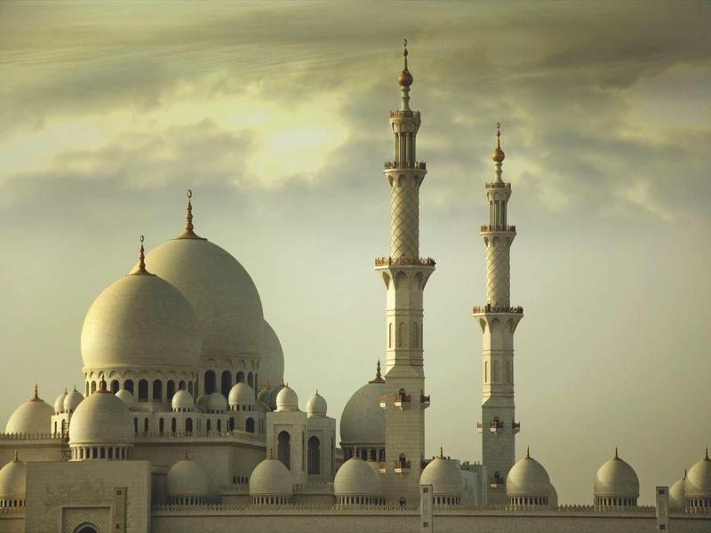 Große Moschee mit drei Kuppeln und zwei hohen Minaretten unter bewölktem Himmel.