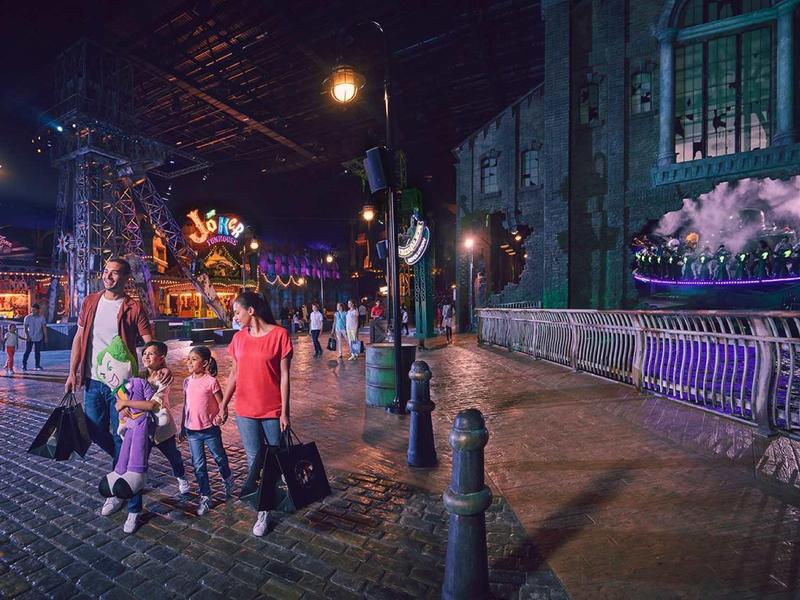 Menschen mit Gepäck laufen nachts über eine gepflasterte Straße neben einem historischen Zug.