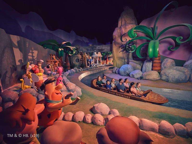 Disney-Parkattraktion mit Menschen in Booten auf Wasserbahn, Felsen und bunt dekorierten Figuren.