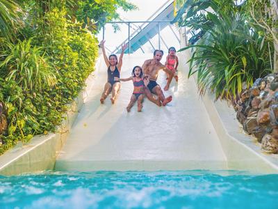 Kinder rutschen zusammen auf einer Wasserrutsche in einem tropischen Hotelpool.