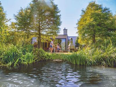 Ein Haus mit Garten grenzt an einen kleinen Teich, umgeben von Büschen und hohen Bäumen.