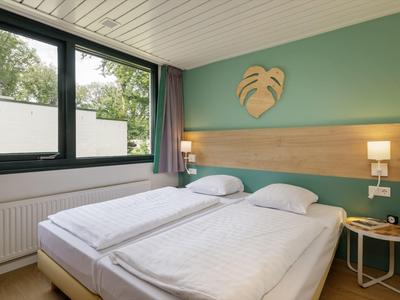 Útulný hotelový pokoj se dvěma jednolůžky, zelenou zdobnou stěnou a oknem.