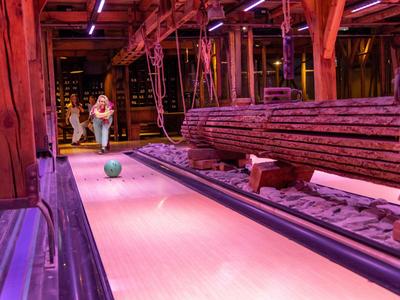 Eine hölzerne Kegelbahn in einem rustikalen Innenraum mit Holzstämmen und roten Beleuchtungselementen.