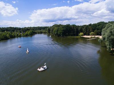 Jezero s loděmi a zalesněným břehem pod modrou oblohou s mraky.