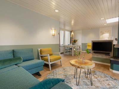 Pohodlný obývací pokoj s pohovkou, křesly, kobercem a televizí v moderním hotelovém pokoji.