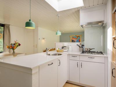 Moderní kuchyně s bílým zařízením, kuchyňským ostrůvkem a zelenými závěsnými lampami ve rekreačním domě.