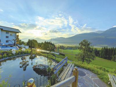 Idylická krajina s rybníkem, horským panoramatem a domy při západu slunce.