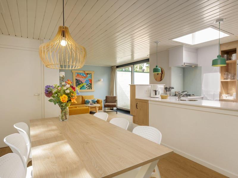 Světlá obytná kuchyně s dřevěným stolem, bílými židlemi a moderní kuchyňskou linkou.