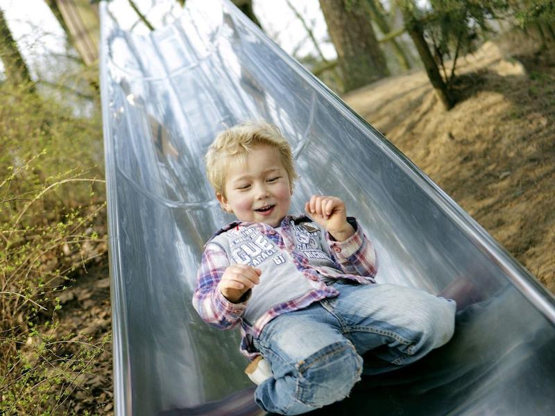 Chlapec radostně sjíždí kovovou skluzavkou v lese.