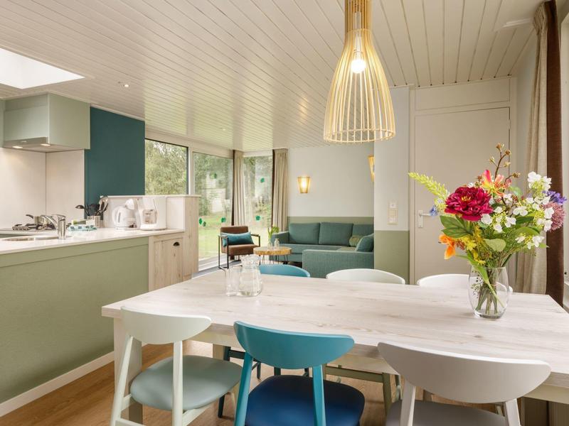 Moderní jídelní část s bílým stolem, barevnými židlemi a výhledem na zelený posezní kout.