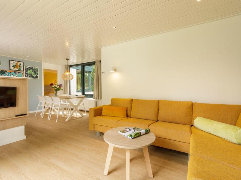 Světý obývací pokoj se žlutou pohovkou, malým dřevěným stolkem a otevřeným jídelním koutem s oknem.