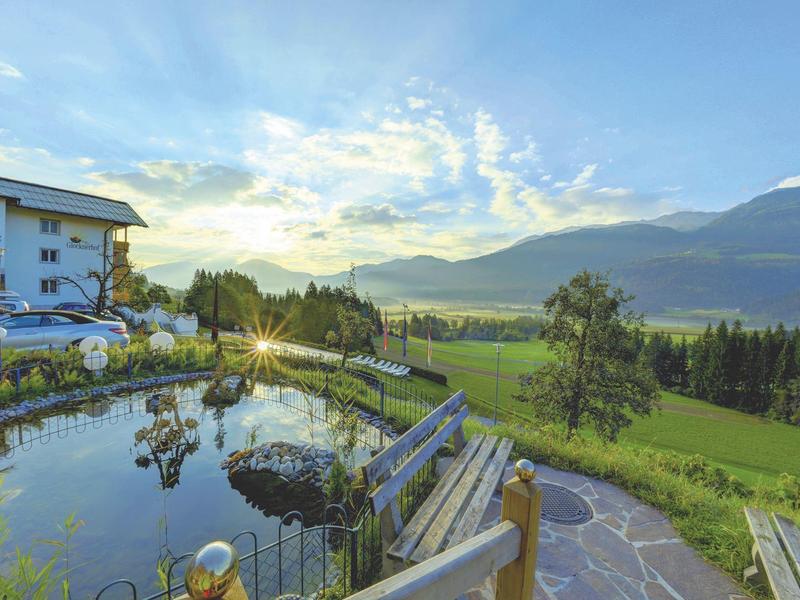 Idylická krajina s rybníkem, horským panoramatem a domy při západu slunce.