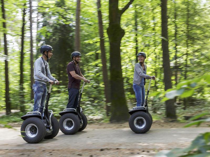 Tres personas montan segways en fila por un sendero boscoso en un parque.