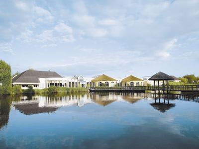 Luxuriöse Hotelanlage mit Bungalows und Steg am ruhigen Wasser unter blauem Himmel
