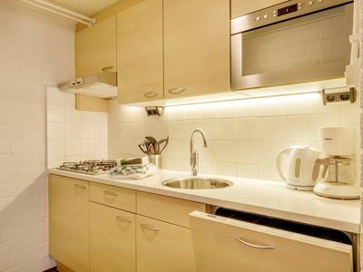 Mała kuchnia z zlewem, kuchenką, ekspresem do kawy i jasnymi szafkami.