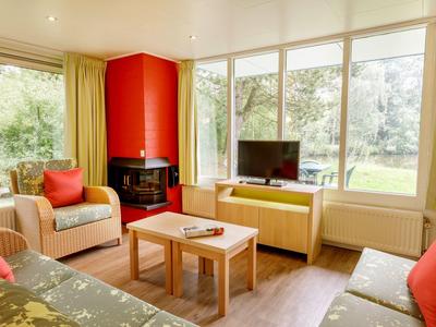 Jasny salon z kominkiem, dużym oknem i wygodnymi miejscami do siedzenia w ciepłych kolorach.