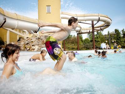 Menschen genießen einen Swimmingpool mit Wasserrutsche bei sommerlichem Wetter.