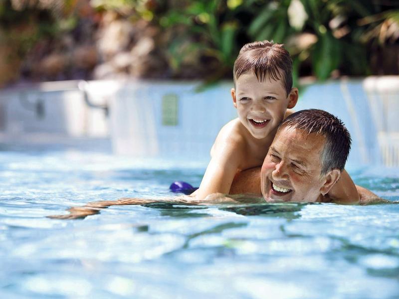 Ojciec i syn śmieją się i bawią w czystym hotelowym basenie.