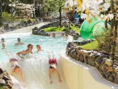 Kinder rutschen in einem Wasserpark, umgeben von Felsen und grüner Landschaft.