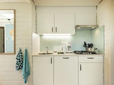 Angolo cottura compatto con mobili bianchi e due asciugamani appesi al muro.