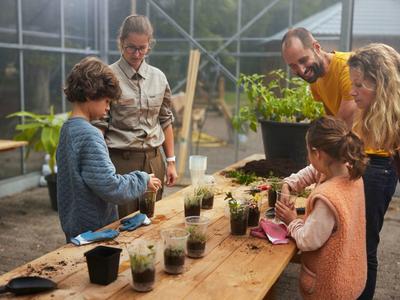 Bambini e operatori piantano piantine su un tavolo di legno in una serra.