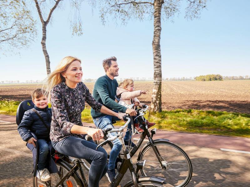 Famiglia con due bambini che pedalano insieme su due biciclette su un sentiero di campagna.