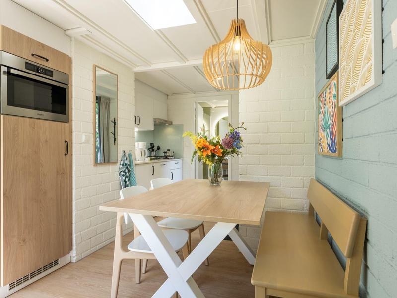 Zona pranzo moderna con panca in legno, tavolo e angolo cottura in una stanza luminosa.