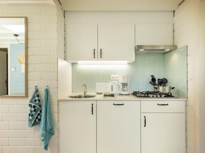 Angolo cottura compatto con mobili bianchi e due asciugamani appesi al muro.