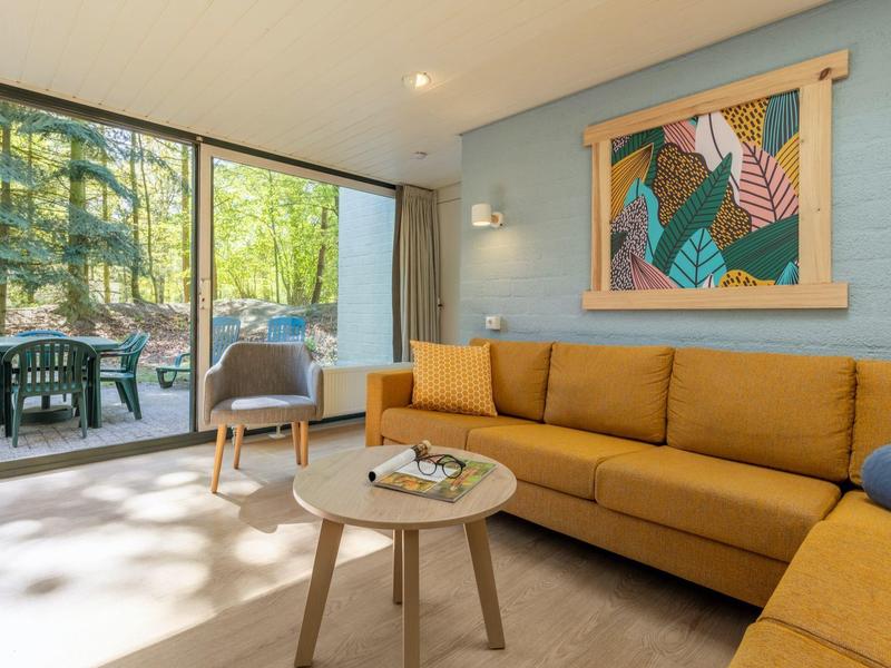 Soggiorno luminoso con tappeto beige, divano marrone, tavolino e porta finestra sul verde esterno.