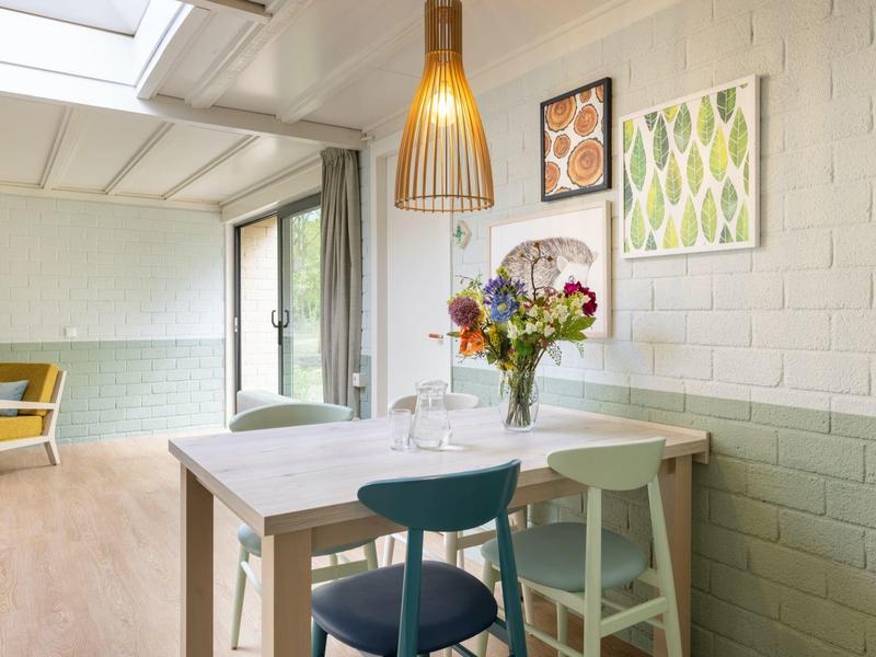 Zona pranzo luminosa con mobili bianchi, sedie blu e composizione floreale fresca.