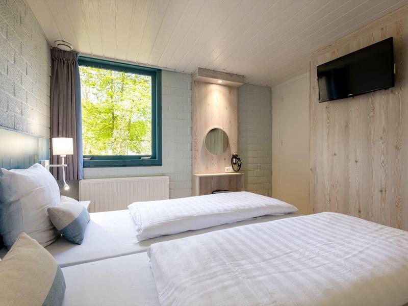 Una camera d'hotel luminosa e moderna con due letti singoli, finestra e TV a parete.