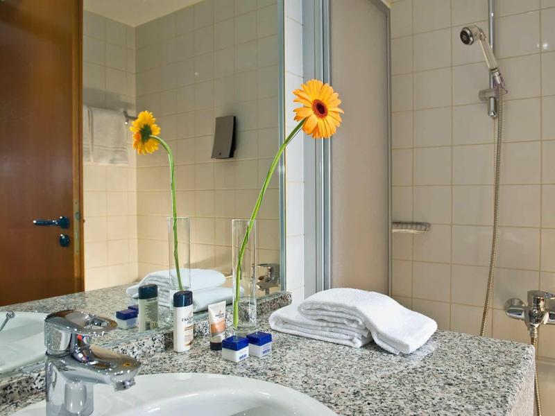 Badezimmer mit Granitwaschbecken, Spiegel, gelber Blume in Vase und weißen Handtüchern.