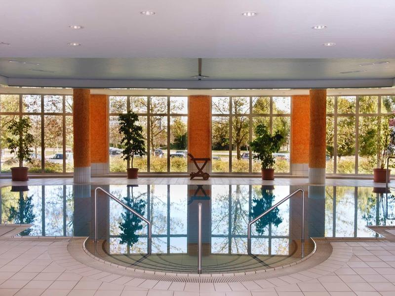 Hell beleuchtetes Schwimmbad mit großen Fenstern und Pflanzen entlang der Rückwand.