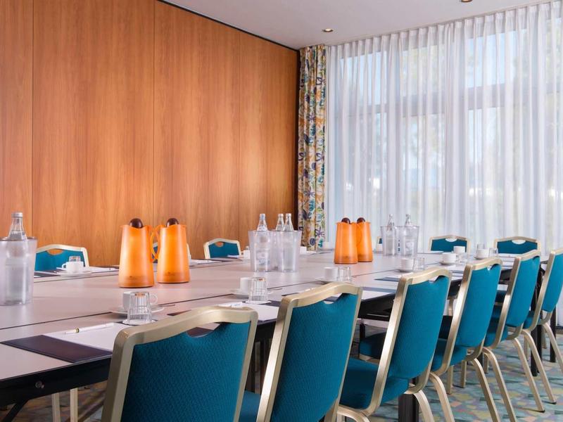 Moderner Konferenzraum mit langen weißen Tischen, blauen Stühlen und orangefarbenen Karaffen.