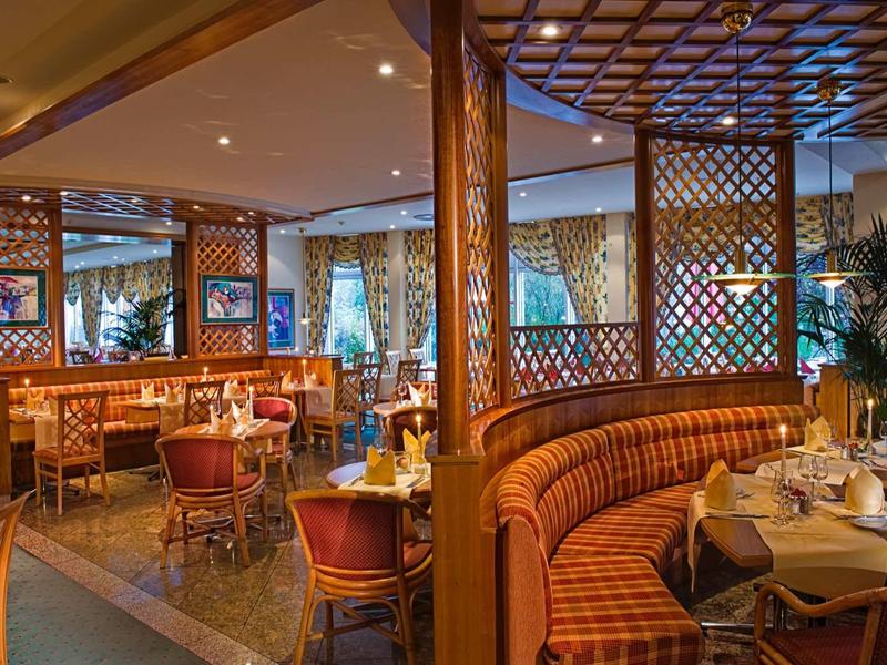 Gemütliches Restaurant mit Holzelementen, runden Tischen und bequemen Polstersesseln in warmen Farben.