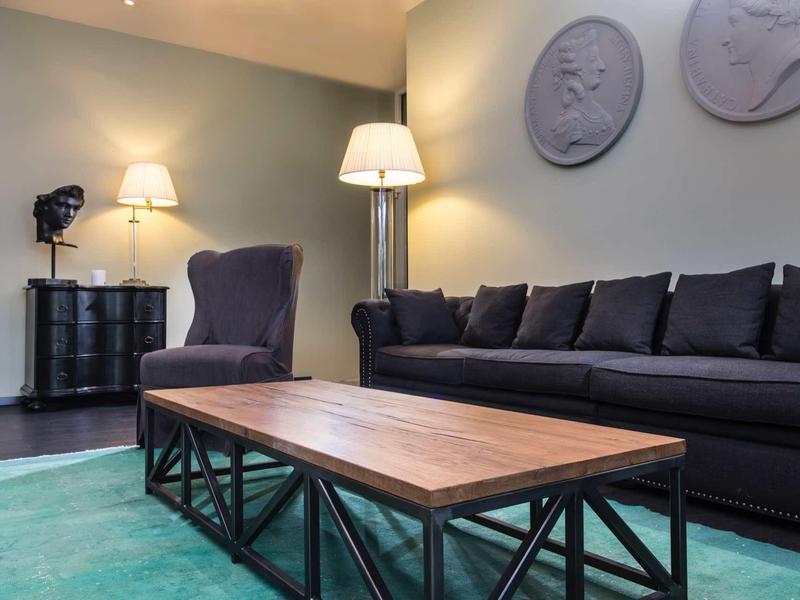 Moderner Wohnraum mit schwarzem Sofa, Holztisch auf Metallgestell und zwei runden Wanddekorationen.