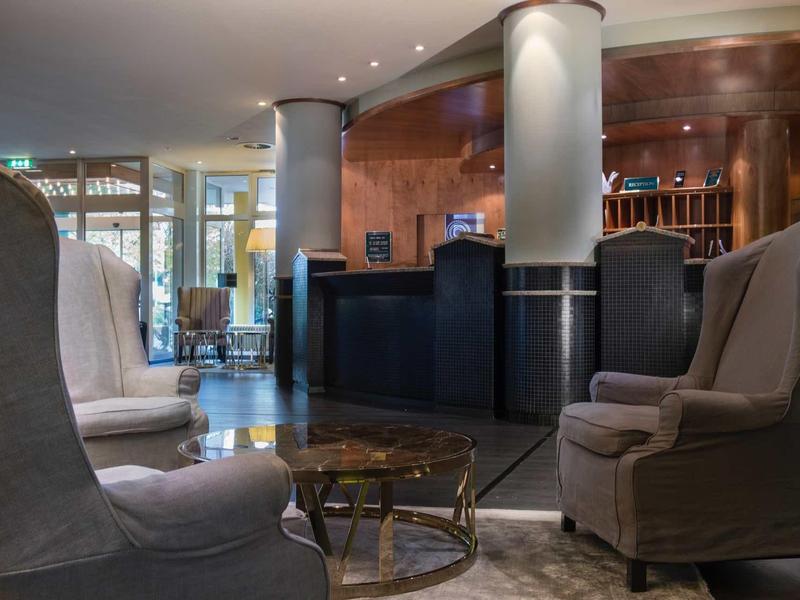 Elegante Lounge mit grauen Sesseln, runden Tischen und einem dunklen Empfangstresen.