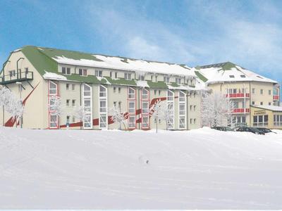 Duży budynek hotelowy z zielonymi dachami, otoczony śniegiem pod niebieskim niebem.