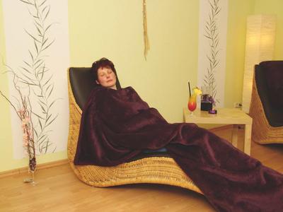 Kobieta relaksująca się na leżaku przykryta kocem w przytulnym pokoju hotelowym.