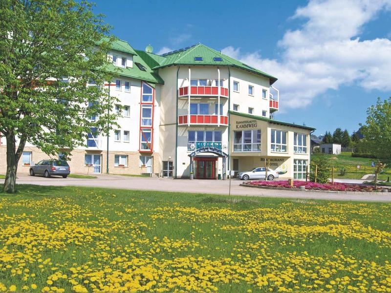 Nowoczesny budynek hotelu z zielonym dachem, otoczony żółtym kwiecistym łąką i niebieskim niebem.