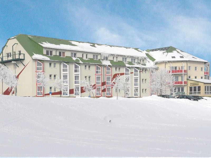 Duży budynek hotelowy z zielonymi dachami, otoczony śniegiem pod niebieskim niebem.