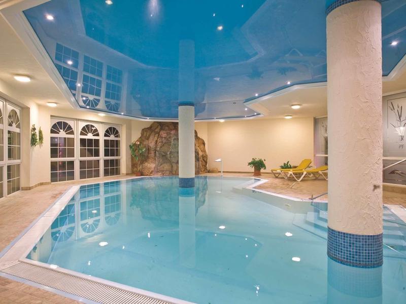 Basen kryty z niebieskim sufitem, kolumnami i leżakami przy krawędzi.