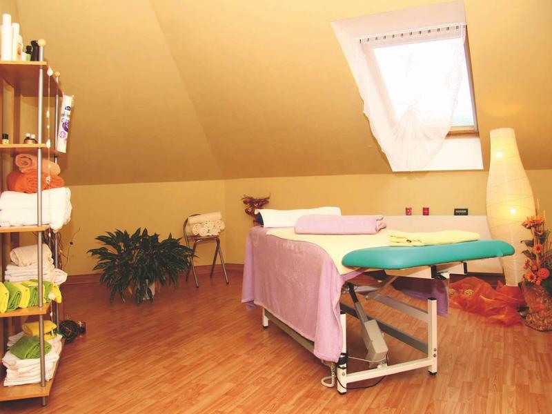 Jasno oświetlone pomieszczenie spa z stołem do masażu, roślinami i półkami na poddaszu.