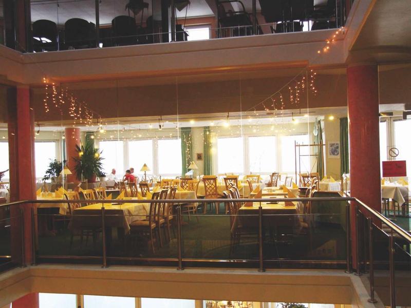 Jasna jadalnia z żółto nakrytymi stołami i dużymi oknami w tle.