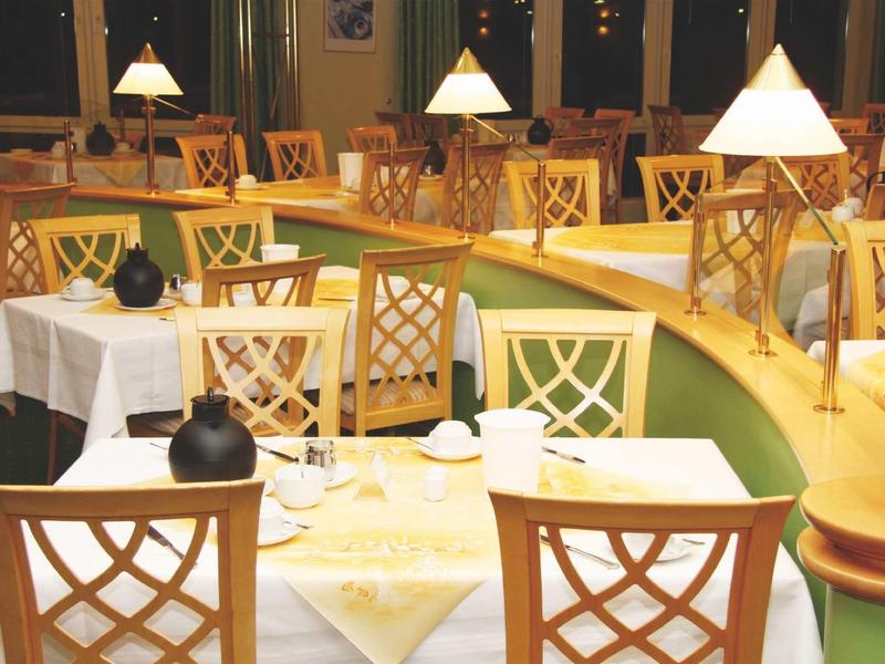 Jasna restauracja z drewnianymi meblami, nakrytymi stołami i ciepłym oświetleniem.