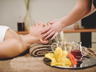 Frau entspannt bei Kopfmassage, Nahaufnahme, Aromatherapie-Öle und Blume im Vordergrund.