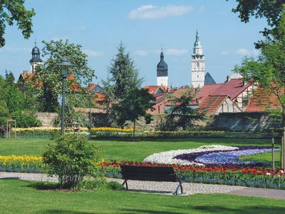 Park mit Blumenbeeten, Bänken und historischen Kirchtürmen im Hintergrund bei klarem Himmel.